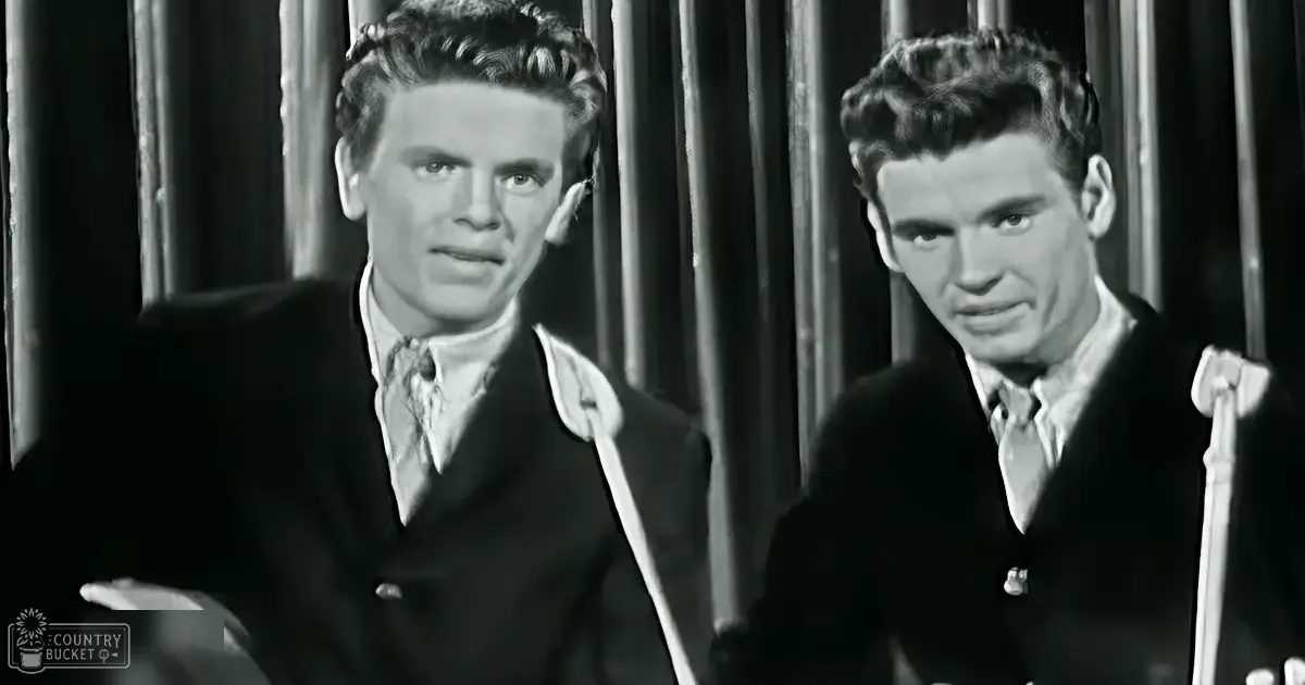 Two young adult males in a theatrical or film setting with formal attire, standing against a backdrop resembling theater curtains.