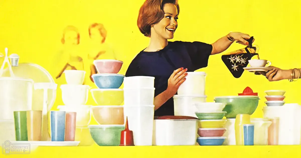 A woman wearing a dark blue dress with short sleeves and holding a floral-patterned teapot, surrounded by colorful kitchenware in an indoor setting with bright yellow walls.