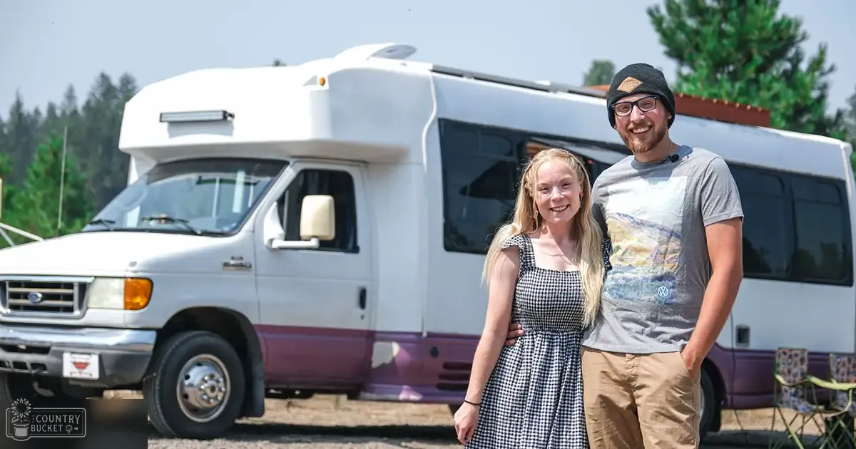 A young adult female wears a sleeveless black and white checkered dress while standing with an adult male wearing a gray 'Volkswagen' T-shirt at a campground near an older Ford RV.