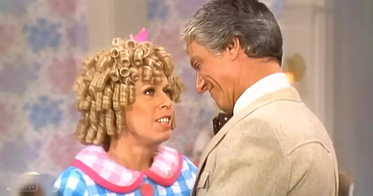 A woman with curly hair in rollers, wearing a blue and white checkered dress indoors.