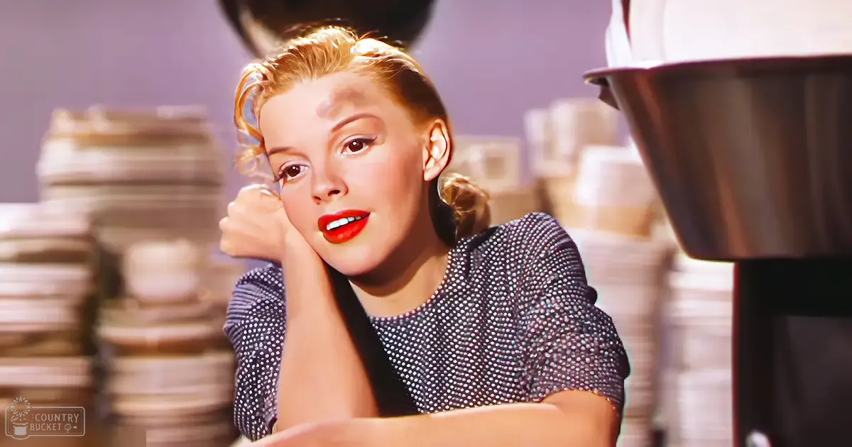 A young adult female wearing a dark blue or black polka dot short-sleeved top with a fitted and form-fitting cut, standing indoors near stacks of disposable cups and saucers in what appears to be a casual dining establishment.