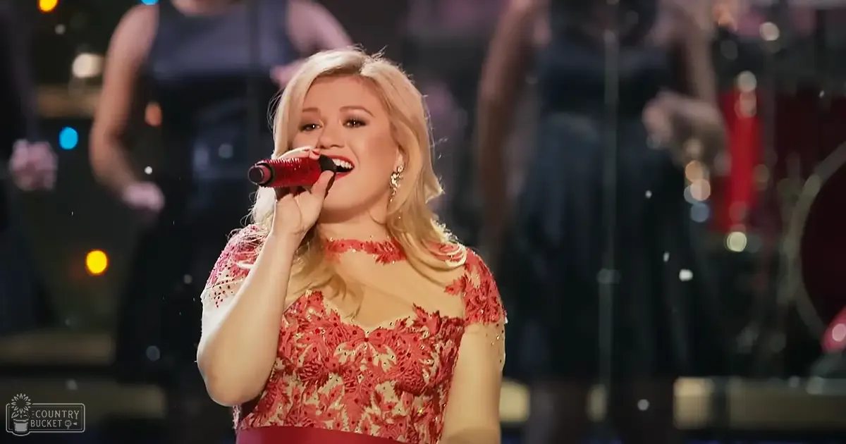 Adult female singer in a red and gold patterned lace dress with large earrings performing on stage at an evening concert.