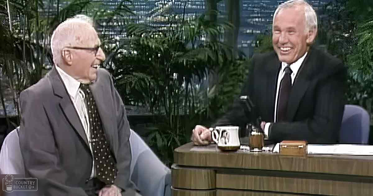 A mid-20th-century talk show set with two adult males in formal attire, seated indoors against a backdrop of greenery and well-lit conditions.