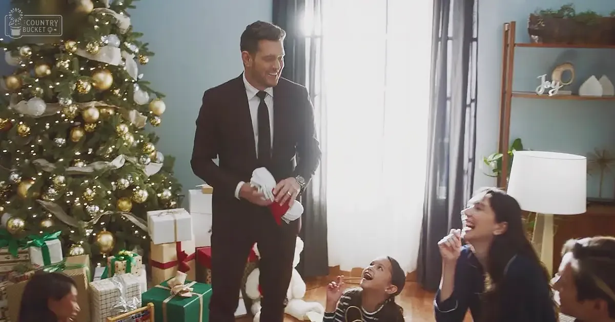 A family scene in a living room decorated for Christmas, with an adult male in a dark suit, children wearing festive attire, and holiday decorations including a Christmas tree and wrapped presents.