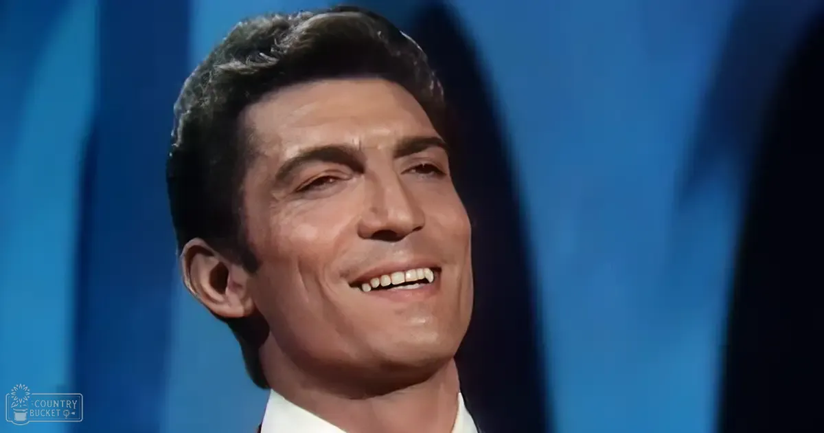 An adult male in a mid-20th-century style white collared shirt and dark suit jacket, set against a simple indoor backdrop with artificial lighting.