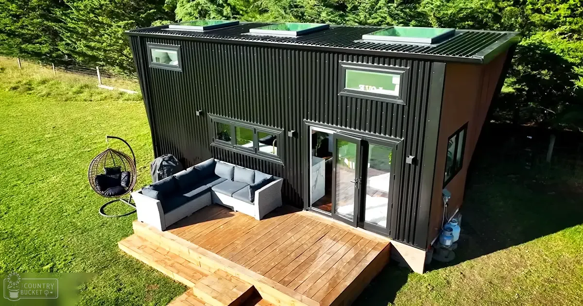 A modern tiny house with a white sectional sofa, black hanging chair, wooden deck in an outdoor grassy setting during daytime.