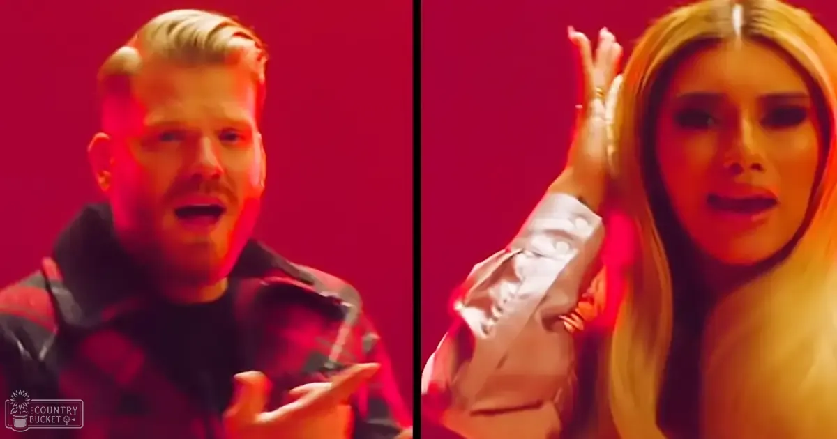 Two adults performing a musical scene indoors with red lighting; one wearing a dark jacket and the other a light-colored top.