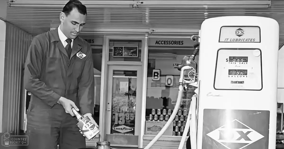 Adult male wearing a dark work uniform with logo patch at an old-fashioned gas station indoors, holding a DX branded canister.