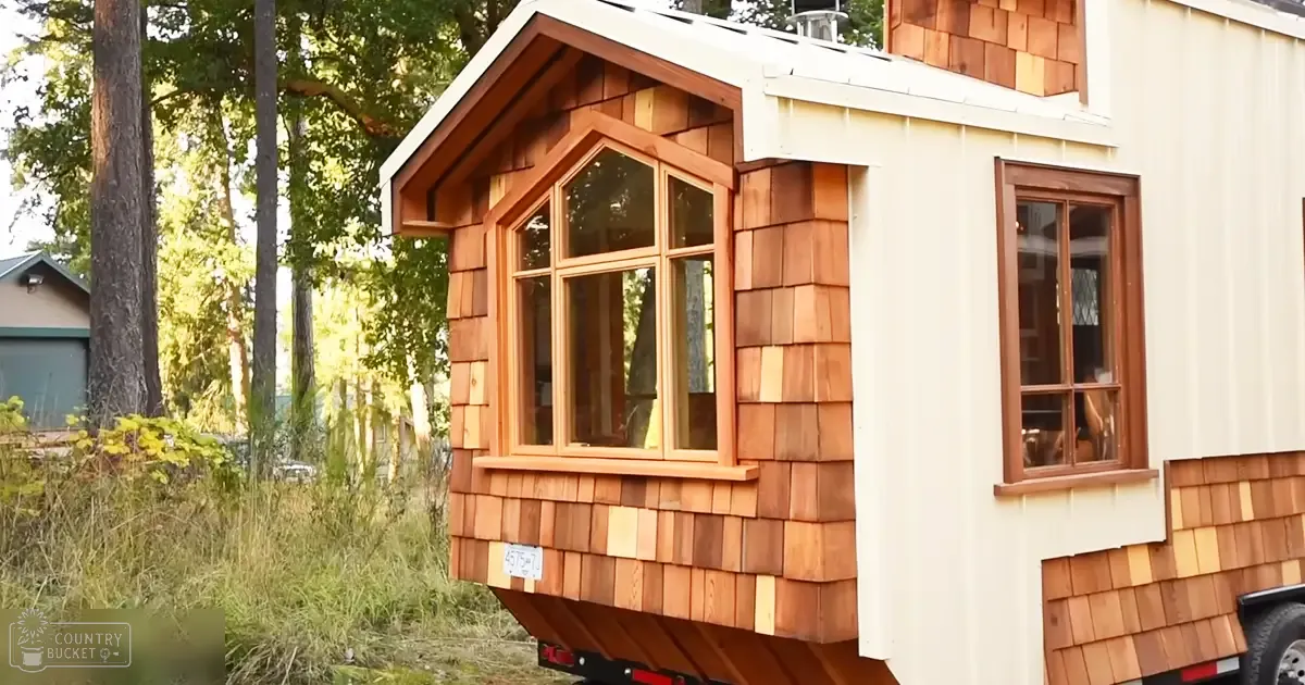 A small wooden house with large windows amidst trees and grass under bright daylight.