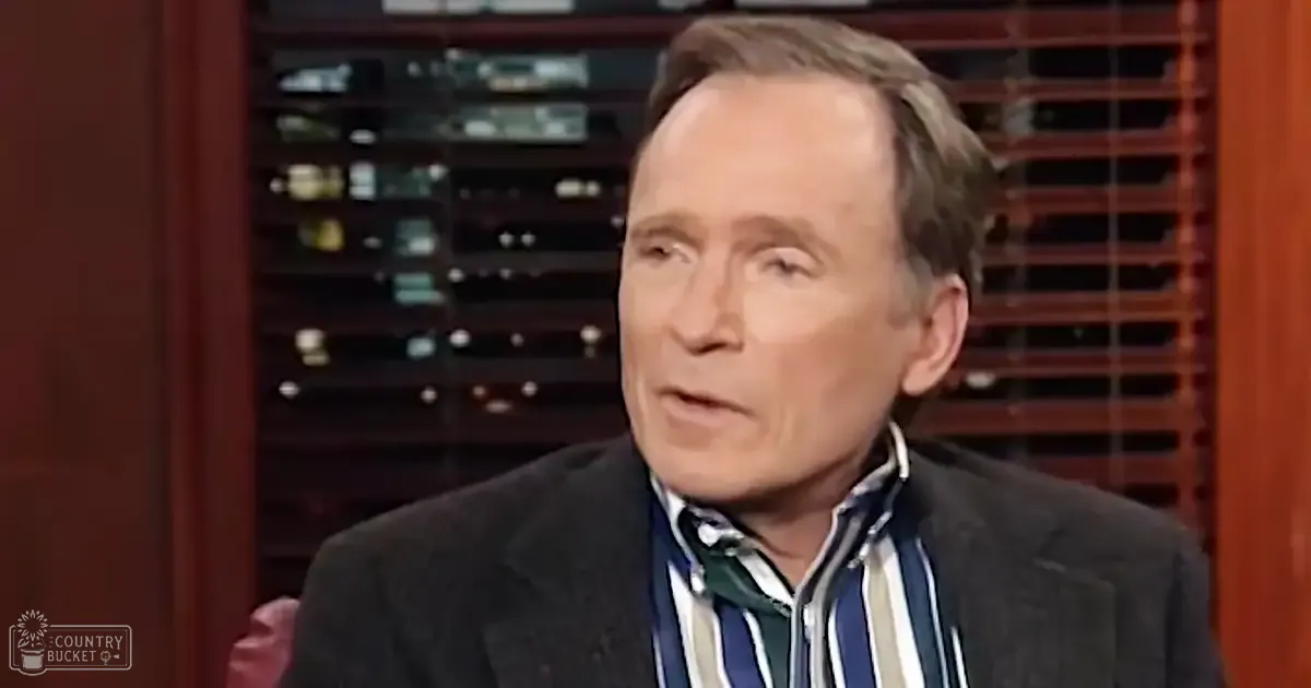 An older adult male wearing a dark blazer over a striped shirt in a studio setting with controlled lighting.