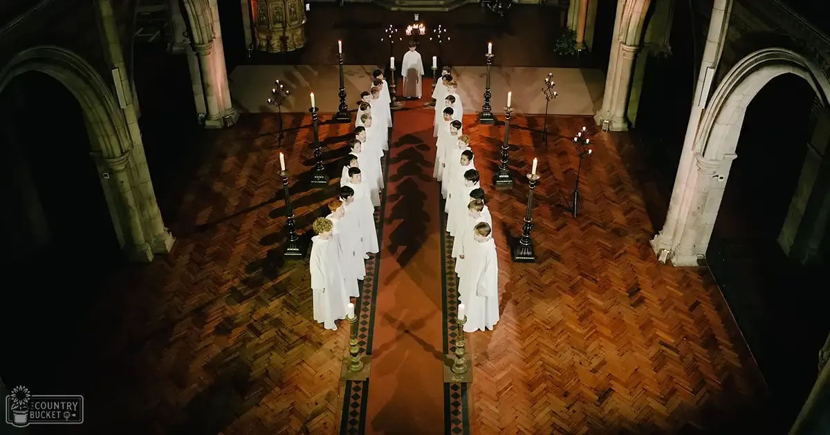 Children in white robes gathered inside a church with wooden parquet flooring, arched doorways, and an altar visible in the background during a religious service or ceremony.