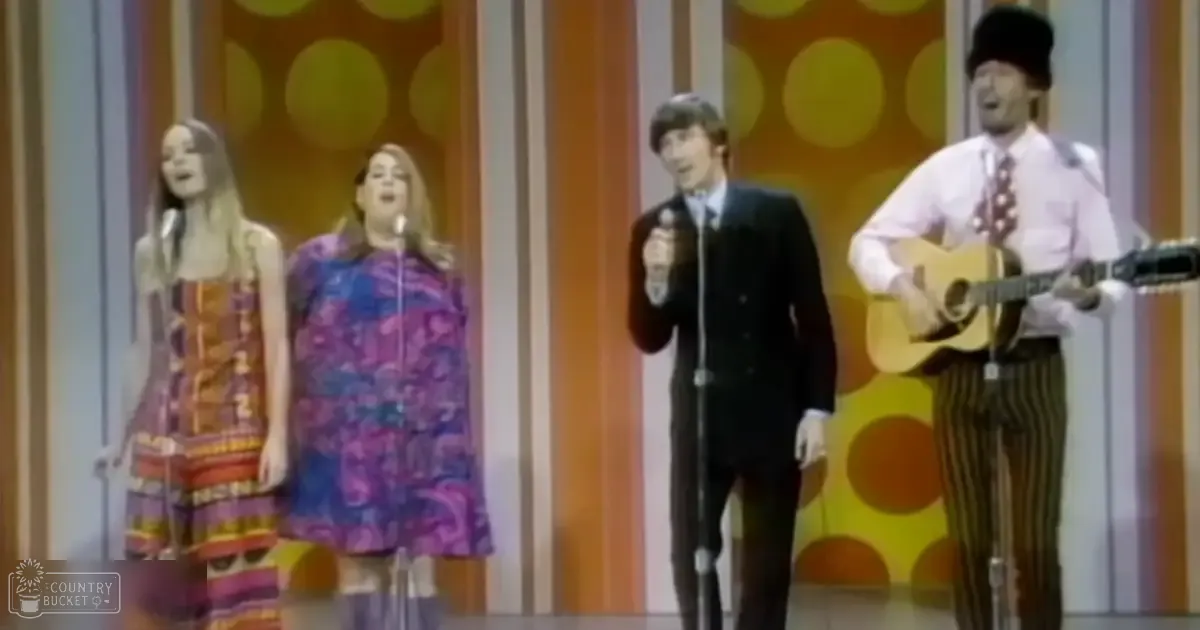 A musical performance with performers wearing vibrant 1960s fashion on an indoor stage set designed to resemble a studio, with vertical panels and large circular patterns.