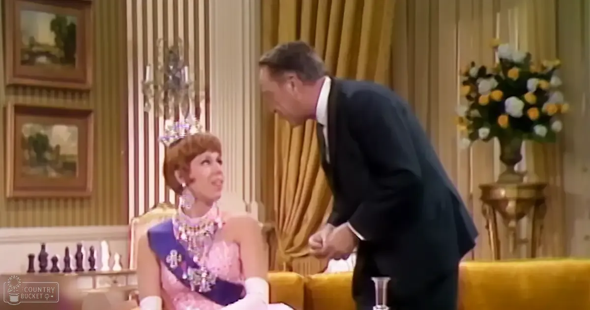 A young adult female wearing a pink and purple mid-20th century dress with intricate detailing and accessories stands beside a middle-aged male in formal attire, both on what appears to be a television show set decorated with furniture and home decor elements.