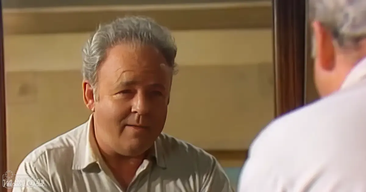 Middle-aged to older adult male wearing a light-colored collared shirt indoors with natural daylight, casual setting.