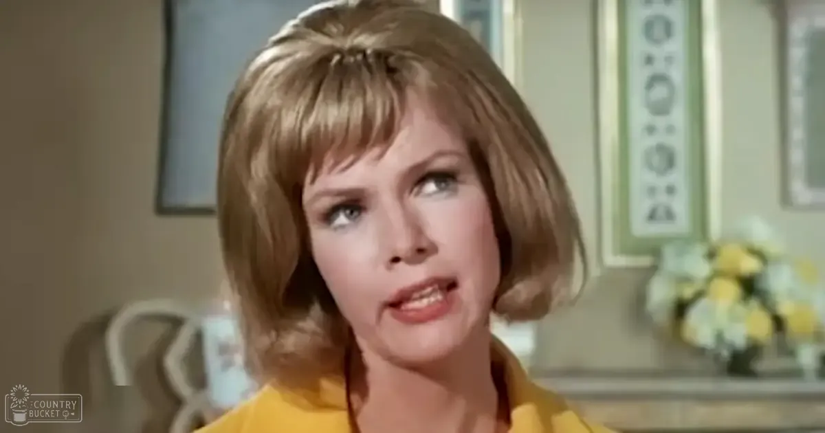 A young adult female wearing a bright yellow, fitted blouse indoors with natural light filtering through.