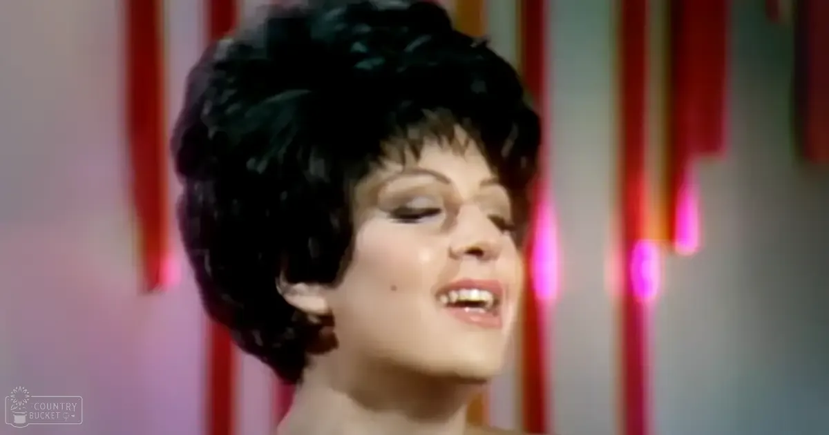 A young adult female sings against a colorful backdrop with vertical red and white stripes and pink lights streaking downward.