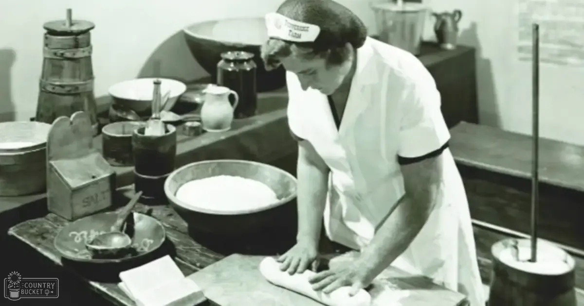 An adult male baker in an old-fashioned kitchen wearing a white apron with black trim, working amidst various baking utensils and ingredients.