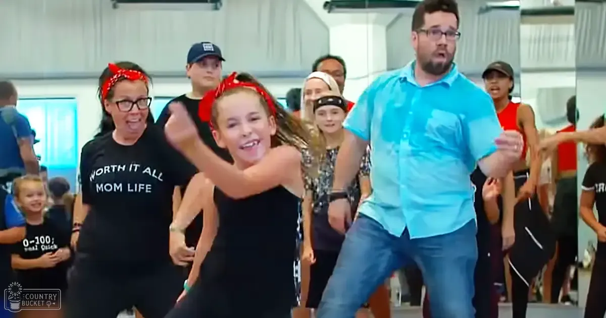 A group dance class with children and an adult male leading or participating, taking place in a dance studio setting during daytime.
