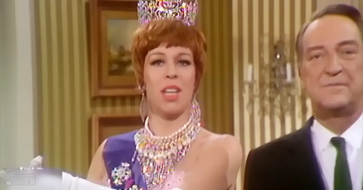 An adult female in a pageant gown with embellishments and accessories, set against striped wallpaper indoors.