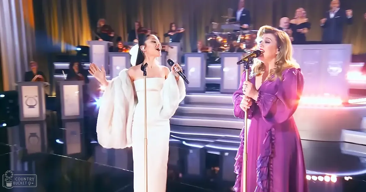 Two adult female singers performing on a formal stage at an evening event with bright spotlights and ornate stage decor.