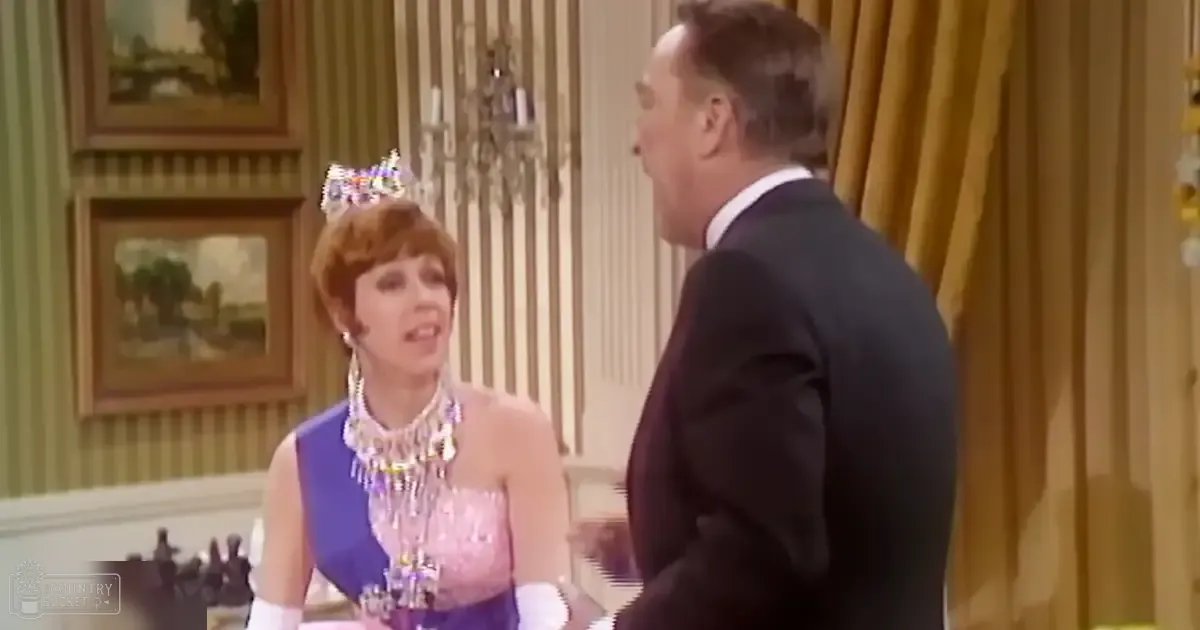 An elegant indoor setting with a woman in an ornate blue and pink dress adorned with beads, standing beside a man in a dark suit jacket and trousers under bright daylight.