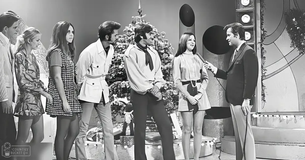 A group of individuals in a 1970s television studio set with artificial stage lighting.