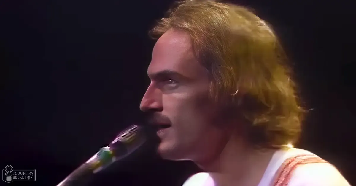 A middle-aged male singer wearing a white tank top with orange stripes, singing into a dynamic microphone at an indoor concert setting.
