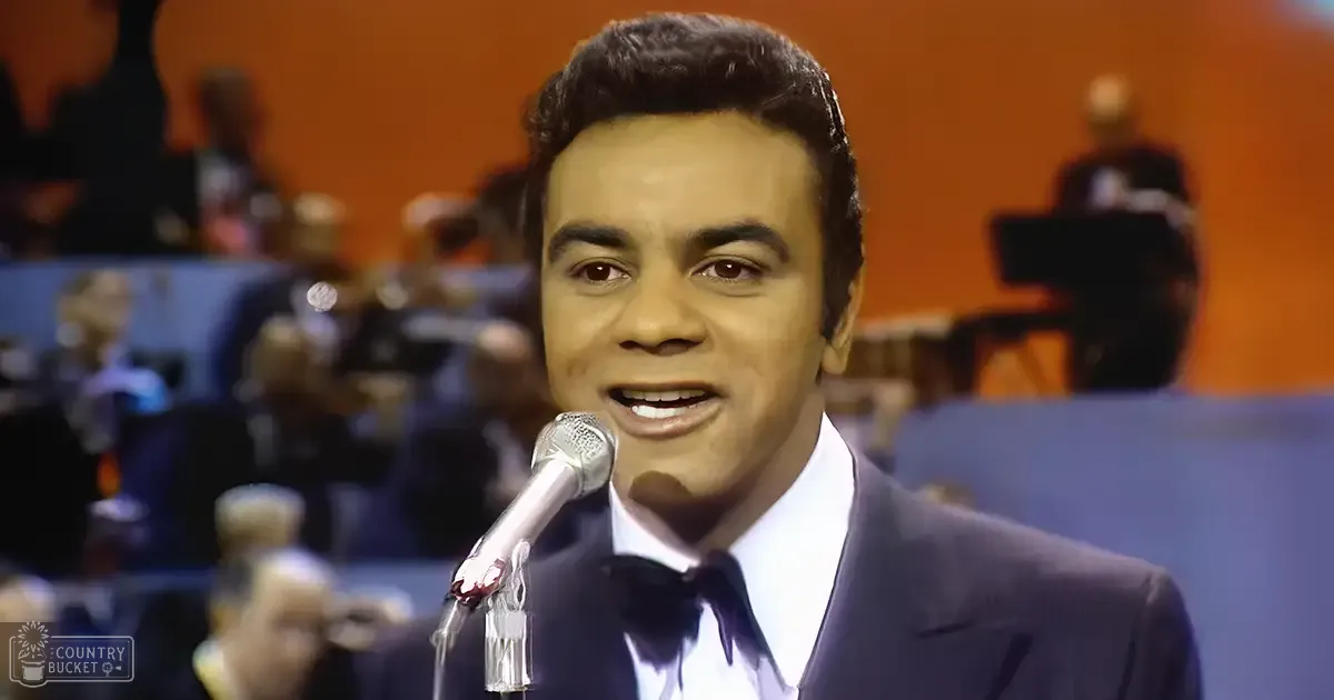 Adult male singer in a dark suit jacket, white shirt with dark tie, performing into microphone in mid-20th century studio setting.