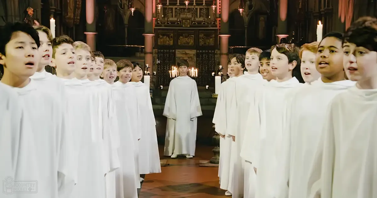 A choir of child male singers in white choir robes performing inside a church with intricate altar decorations during daytime.