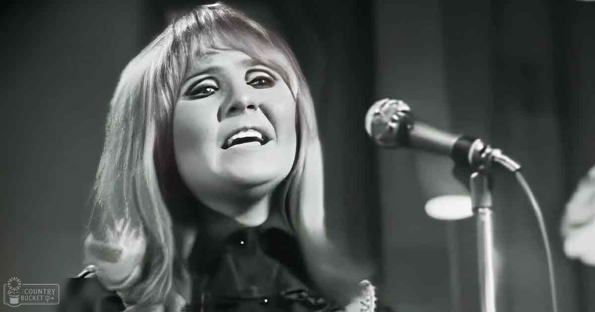 A young adult female in a mid-20th-century style top performs on an indoor stage with curtains, under dramatic lighting.