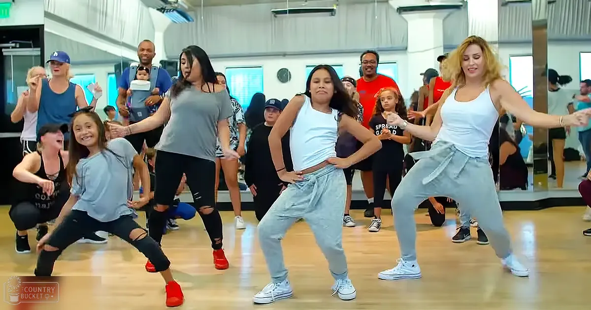 A dance class in progress at a fitness studio with various participants and mirrors reflecting the scene.