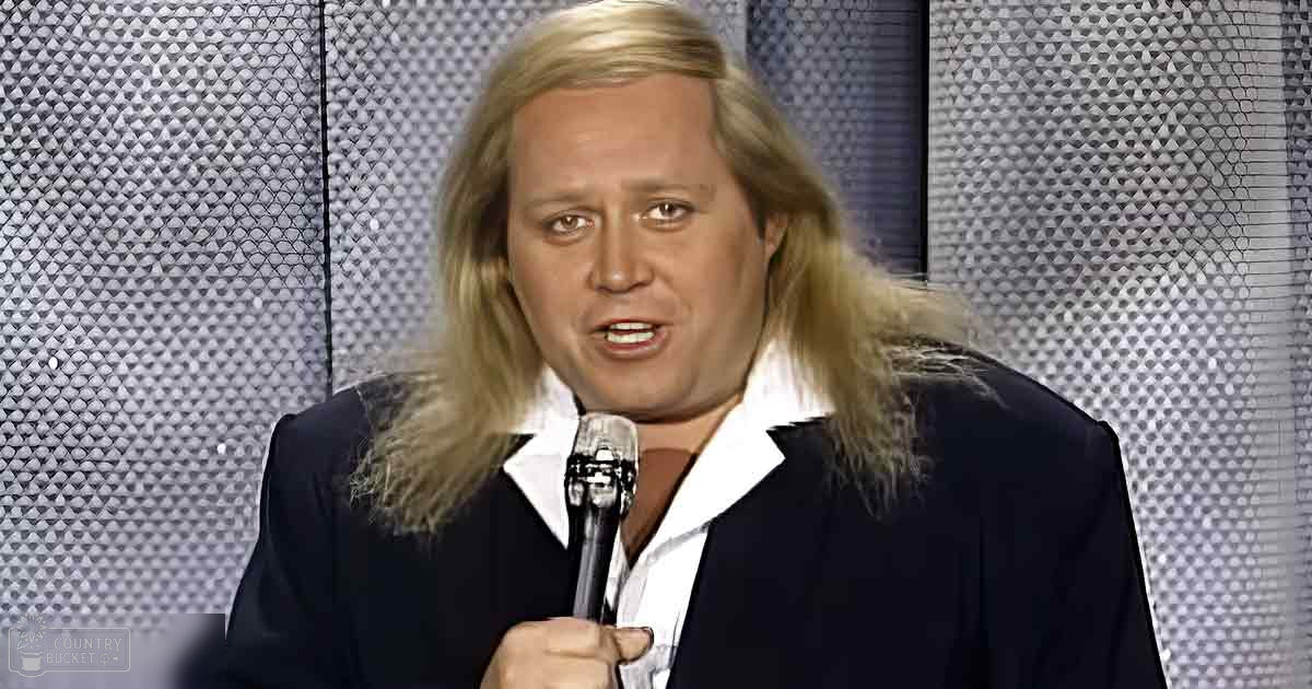 A middle-aged male singer wearing a dark blazer over a white shirt, holding a microphone on an indoor stage with diamond-patterned decor.