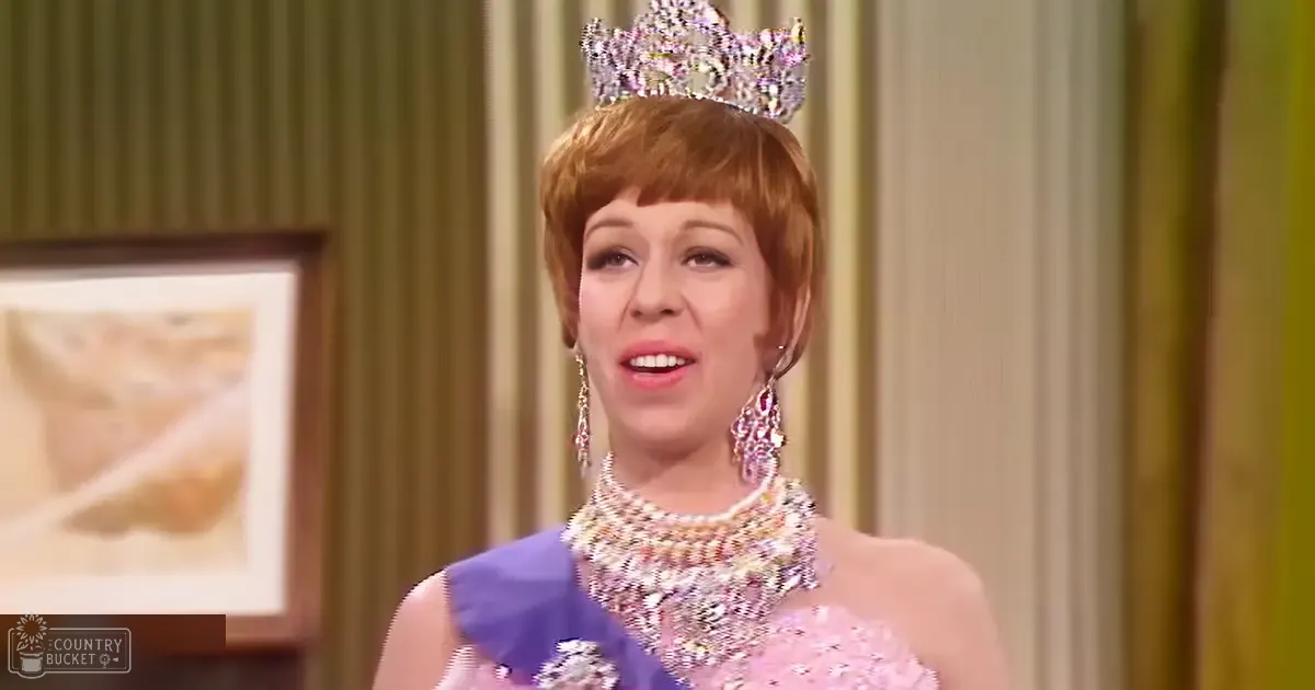 A middle-aged woman in a formal setting wearing a tiara, earrings, and necklace with intricate designs; she is dressed in a pink gown with purple accents.