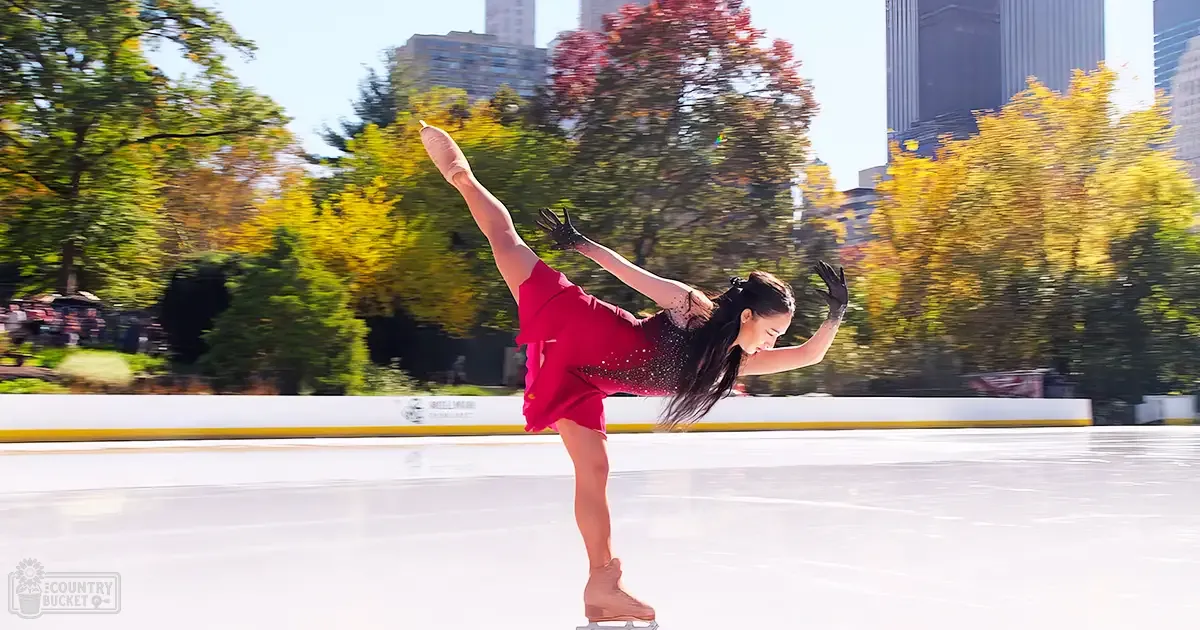 A young adult female figure skating in an outdoor ice rink surrounded by autumn trees, Central Park.