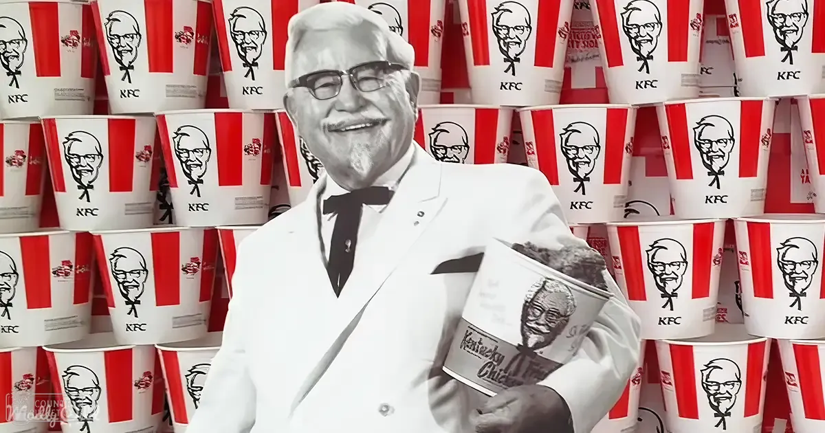 Colonel Sanders in a white suit with KFC buckets behind him, promoting the brand.