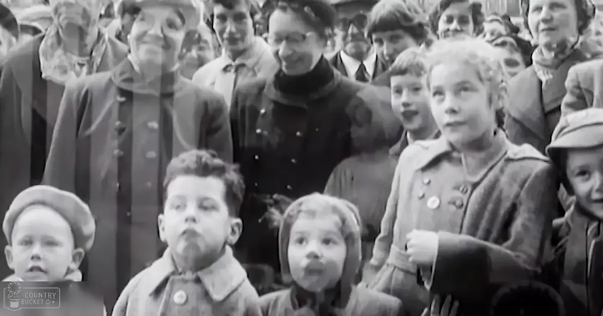 A group of children in an outdoor setting during a public event or gathering, wearing coats typical for the era, standing close together with overcast daylight and dense crowd.