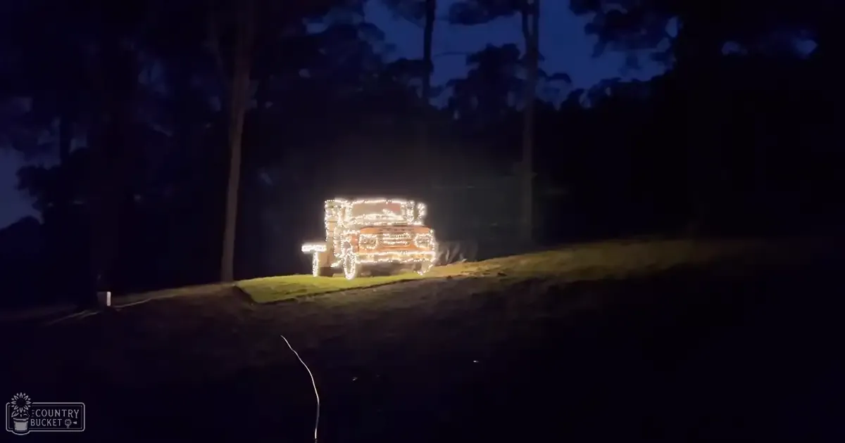 A vehicle covered in bright white and yellow lights, set against a dark nighttime outdoor backdrop with trees.
