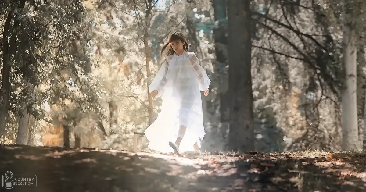 A young girl in a white dress with puffed sleeves and sneakers walks through an autumn forest, surrounded by tall trees and fallen leaves.