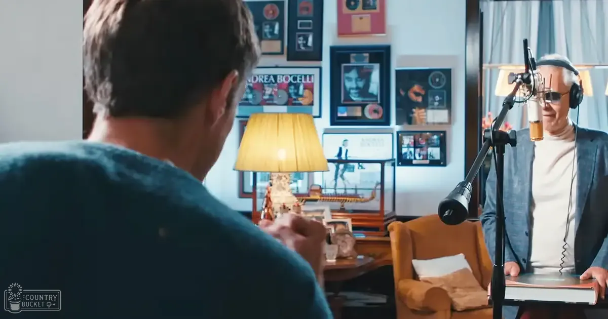Indoor recording studio scene with two adults, one holding a script, surrounded by furniture and home decor, diffuse lighting suggests daytime or well-lit artificial light.