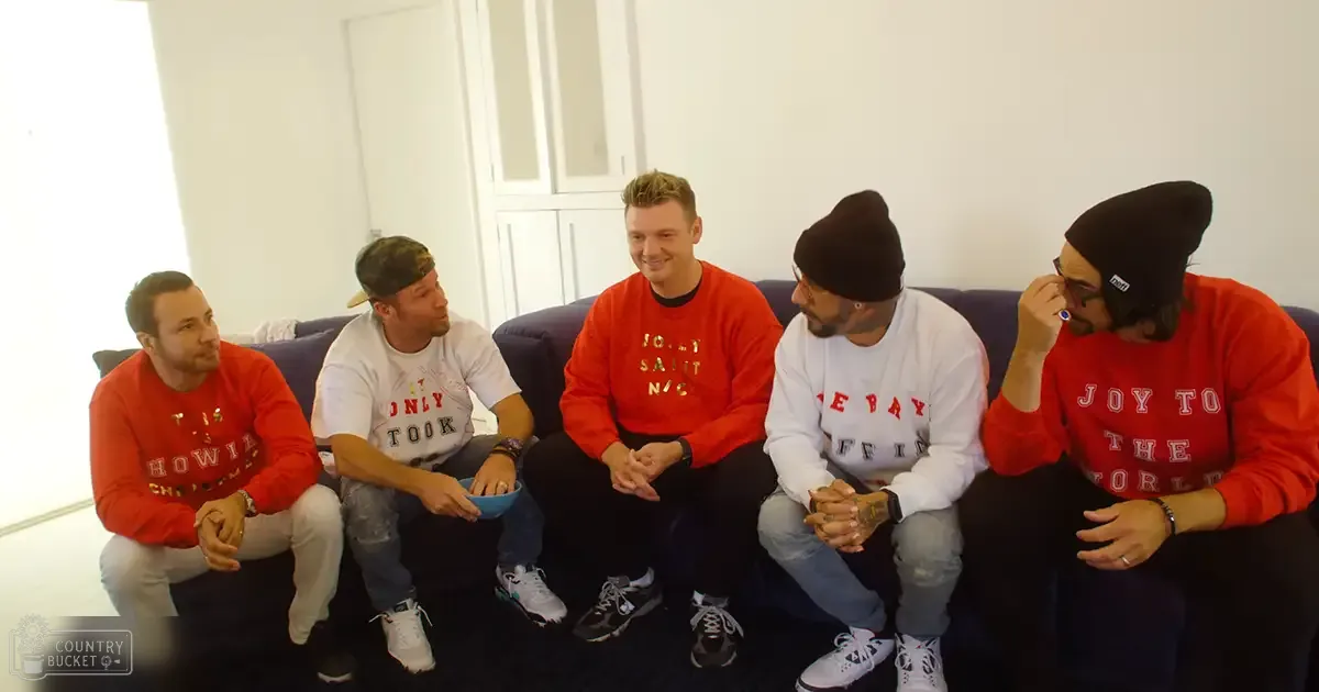 Young adults seated indoors in a casual gathering, wearing sweatshirts with holiday messages and casual attire.