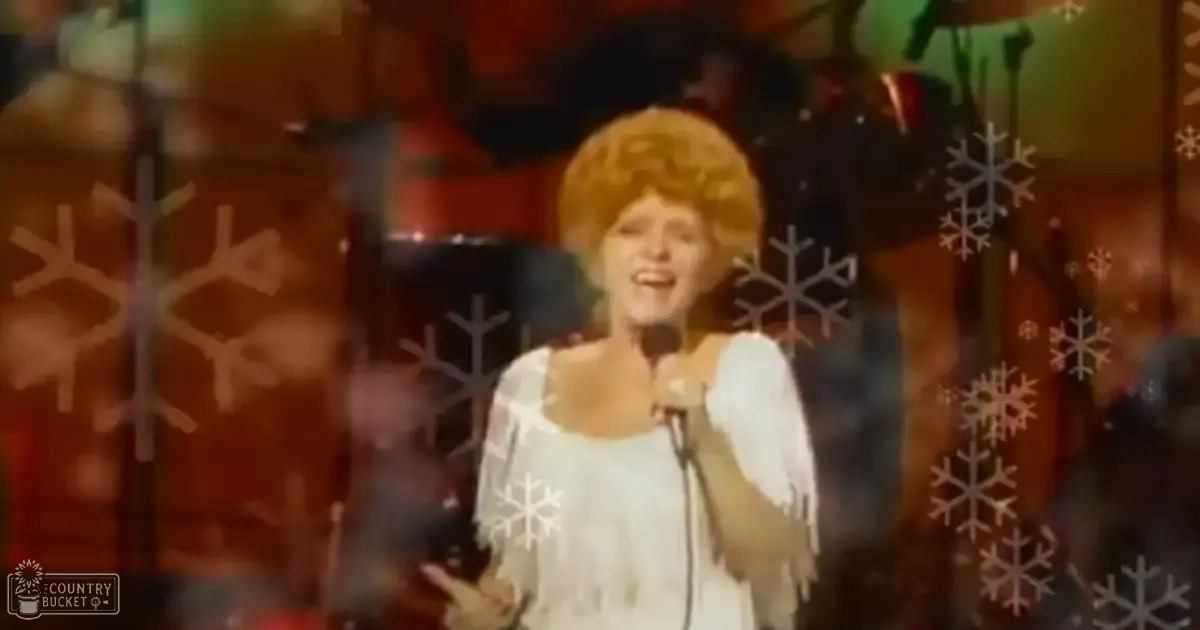 A female performer wearing a white 1950s-style dress with short puffed sleeves and holding a microphone stands on stage under warm-toned lighting.