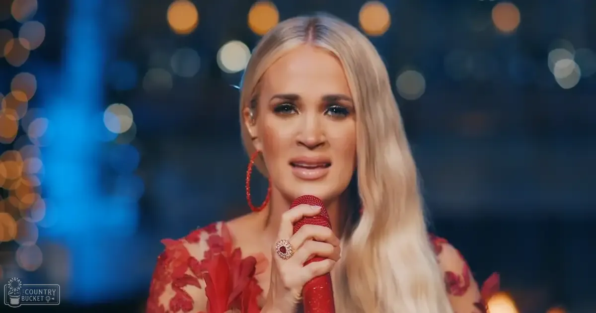 A young adult female in an indoor setting with festive lighting, wearing a floral-patterned off-the-shoulder top and accessorizing with large hoop earrings and a red gemstone ring.