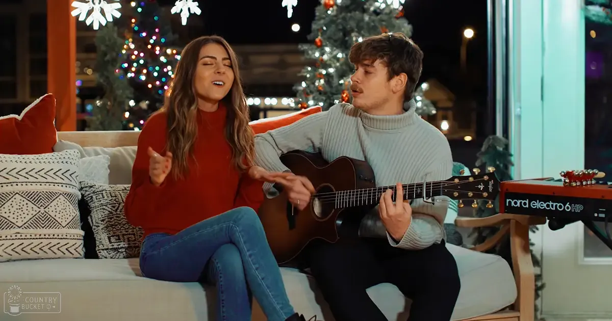 A young adult couple enjoys music together in a cozy living room decorated for Christmas, with patterned throw pillows and a Nord Electro 6 HP keyboard visible.