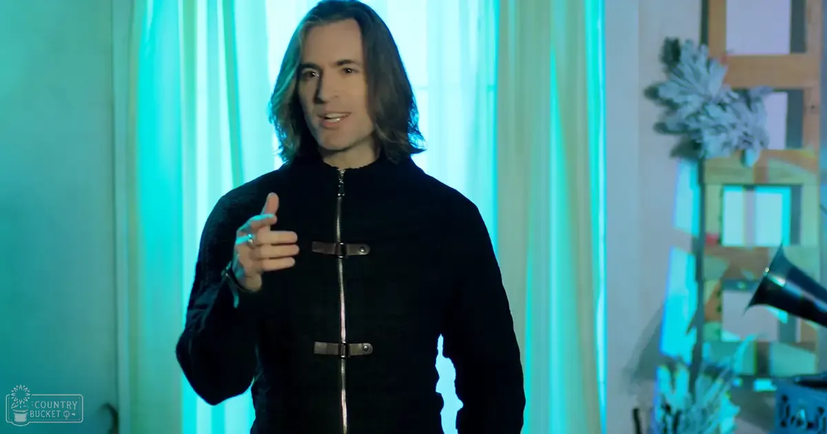 A young adult male wearing a black zip-up jacket with silver buckles stands indoors under modern, futuristic lighting.