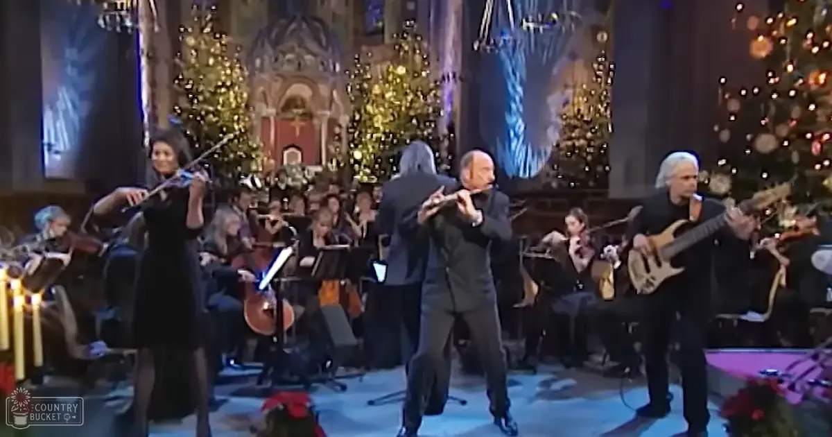 A festive musical performance with musicians in formal attire, Christmas decorations and a chandelier in an ornate indoor venue.