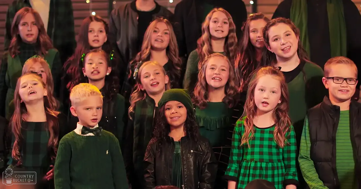 A children's choir in a performance setting with dark curtains and stage lighting at an indoor event during the evening or night.