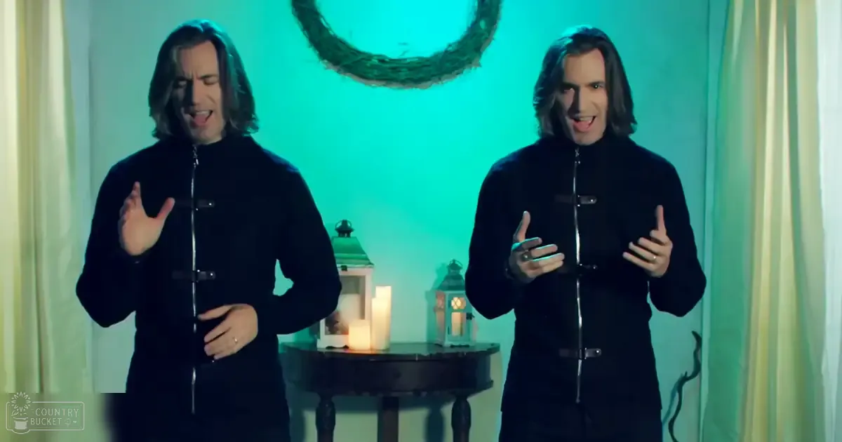 Two adults in a staged setting with traditional-style black garments, silver buttons, rings, vintage lanterns, and a festive wreath indoors.