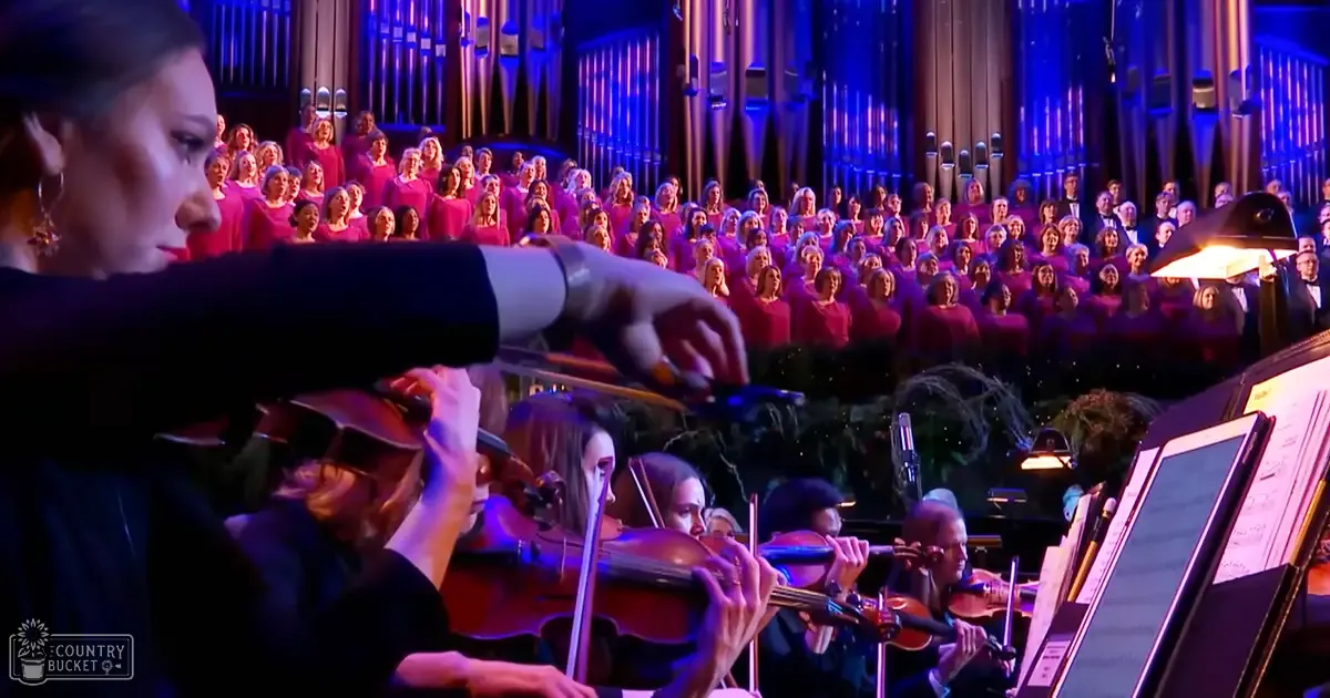 A conductor leading an orchestra with a choir at a concert hall during winter, with dark blue lighting.