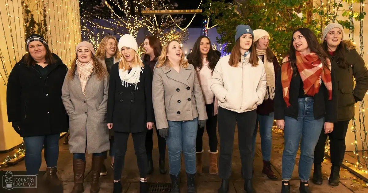 A group of women gathered outdoors in a festive Christmas setting with string lights and decorations, dressed warmly for winter.