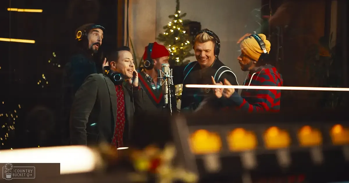 A group of musicians in a recording studio during Christmas time, with a festive tree and holiday lights in the background.
